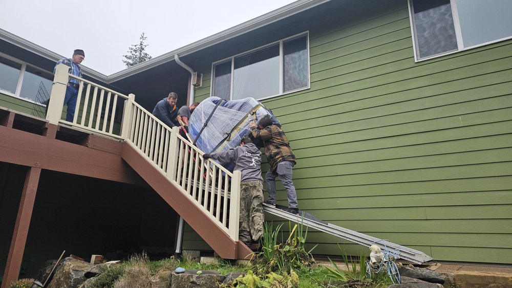 Crew guiding a wrapped grand piano up a residential staircase