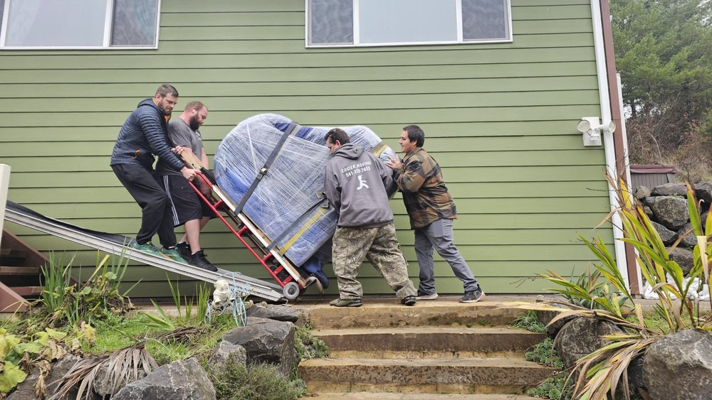 Movers pushing a wrapped piano up outdoor stairs on a dolly