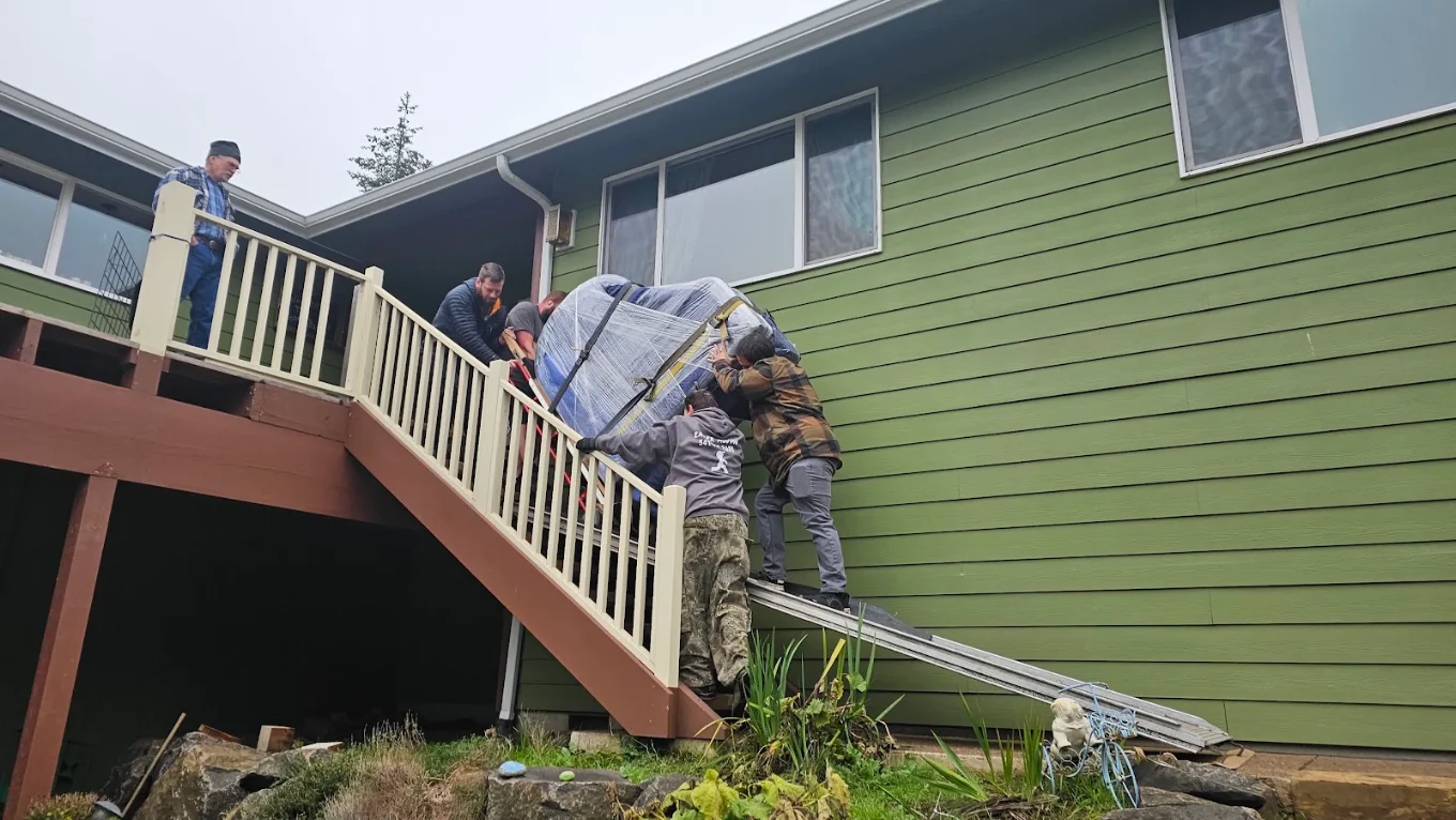 Crew guiding a wrapped piano up a deck stair rail on a ramp